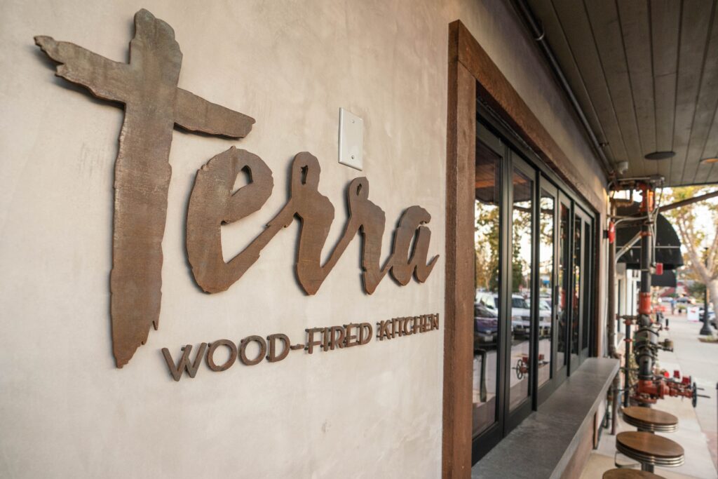 architectural collaborators visioneering studios helped terra wood-fired kitchen. photo featuring pizzeria signage on the exterior of the building