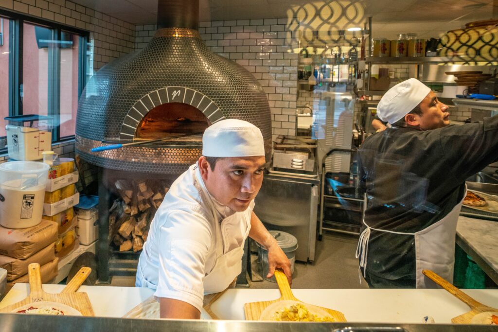 terra wood-fired kitchen pizza chef preparing a pizza to go into the wood fire oven